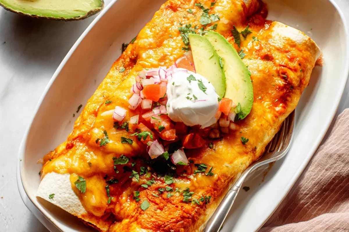 baked breakfast enchiladas with melted cheese topped with avocado sour cream and fresh herbs