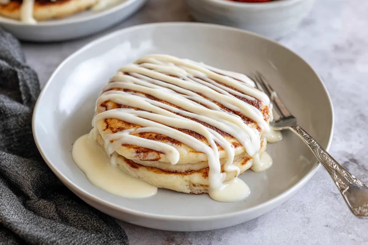 Cinnamon roll pancakes drizzled with cream cheese icing on a plate