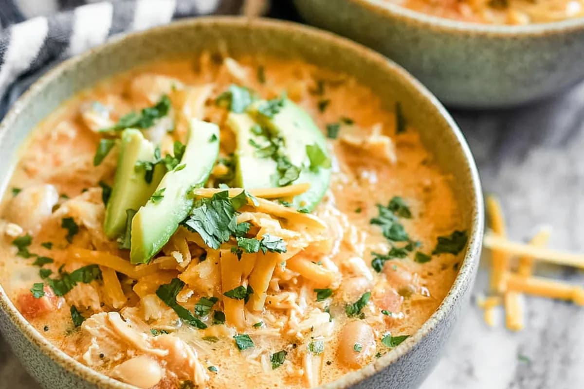Creamy white chicken chili topped with avocado, shredded cheese, and fresh cilantro in a cozy bowl