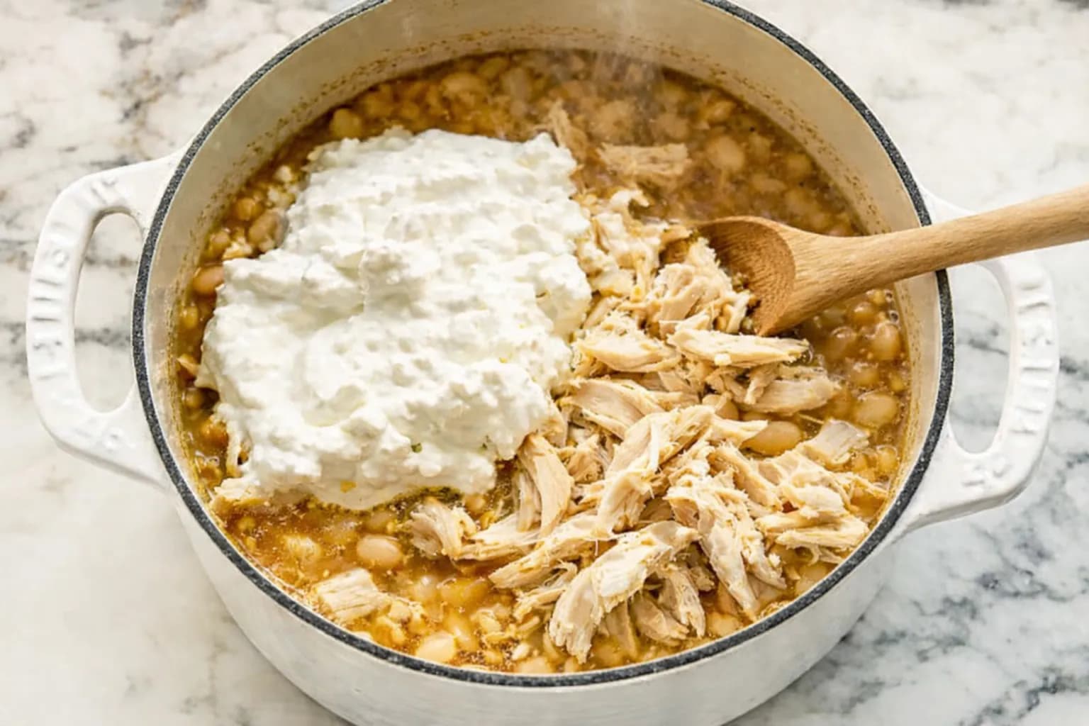 Shredded chicken and sour cream added to creamy white chicken chili before stirring