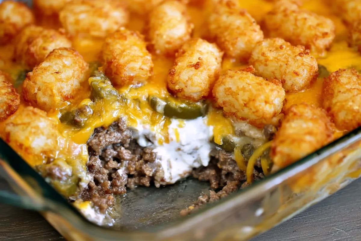 Golden baked tater tot casserole with ground beef, green beans, cheese, and mushroom sauce in a glass dish.