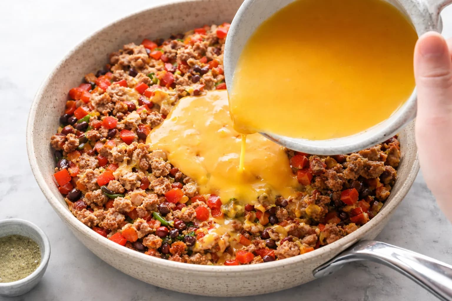 eggs being poured into sausage and vegetable mixture for breakfast enchiladas
